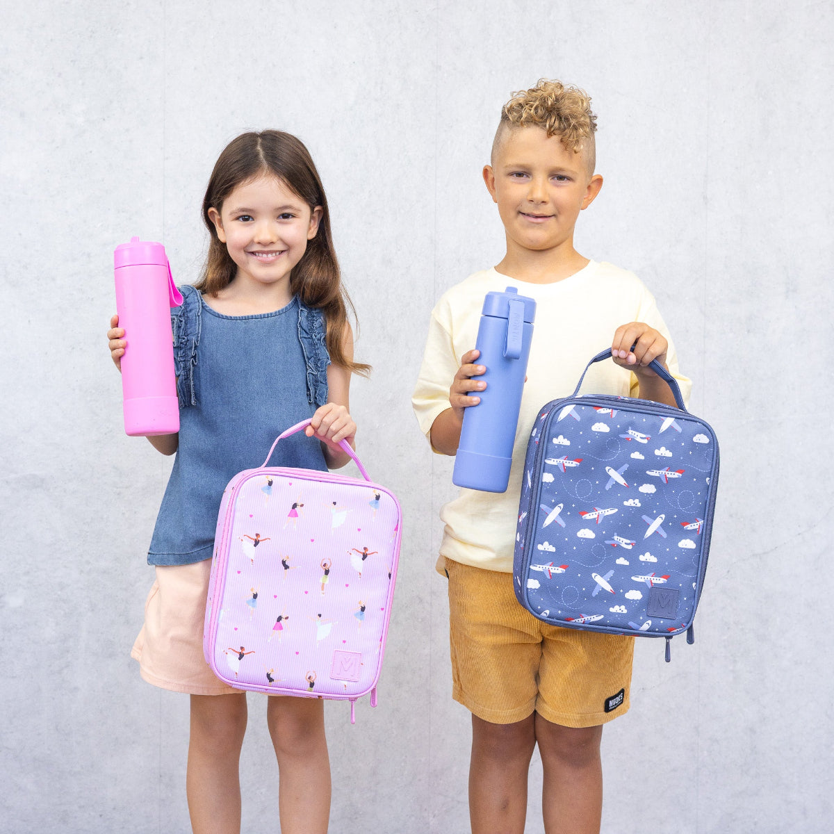 Two children holding colorful lunch bags and water bottles against a plain background