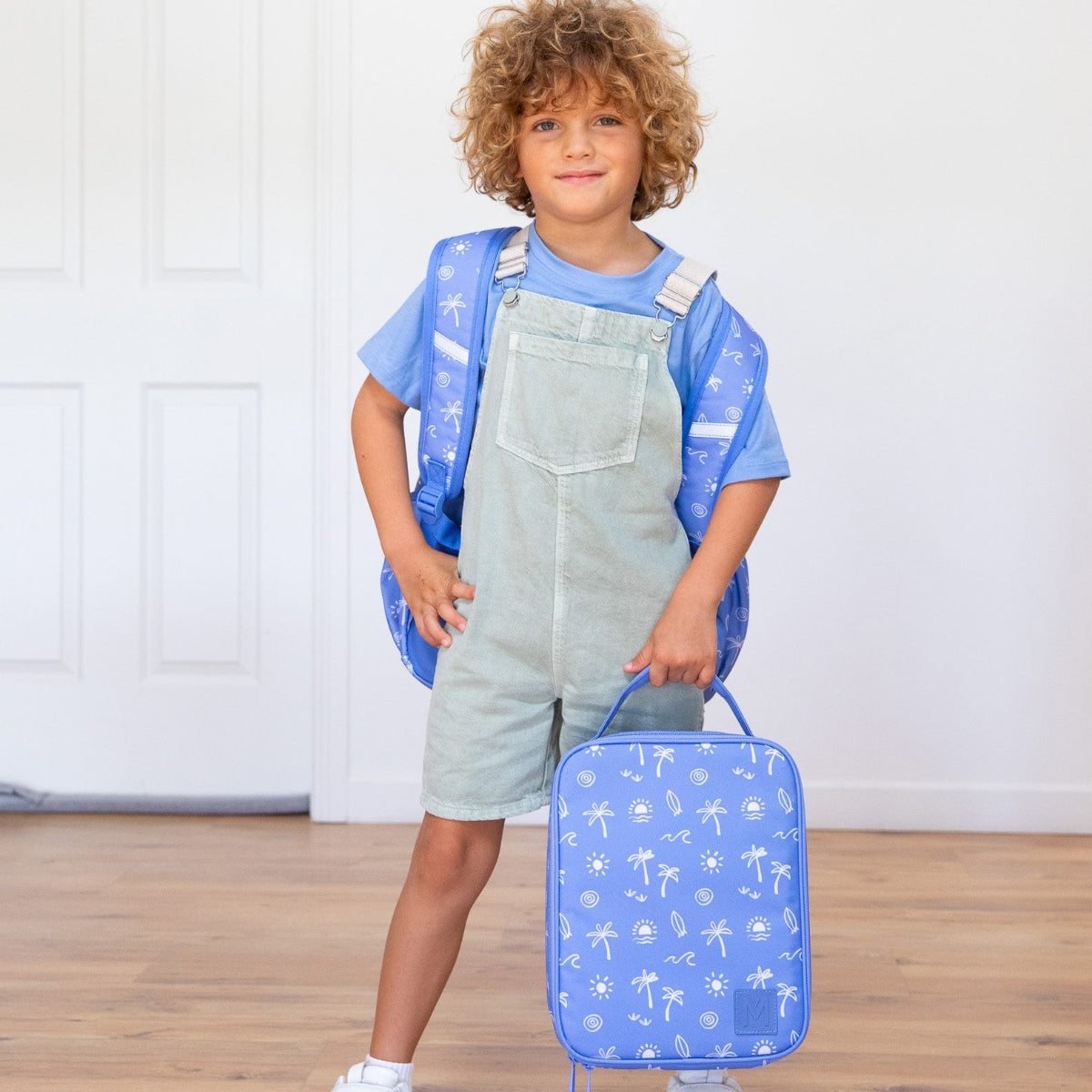 Child holding a blue suitcase with white patterns on a wooden floor.