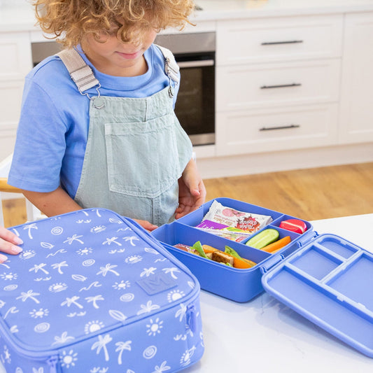 Child in a kitchen with a blue bento box and lunch bag