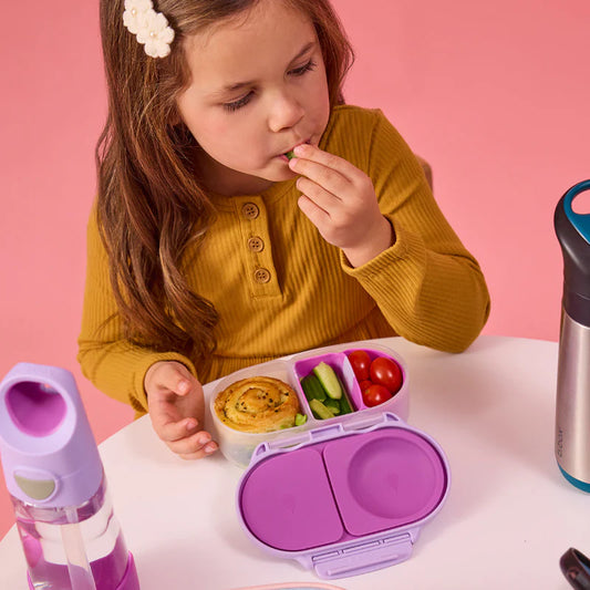 Child eating from a lunchbox with a pink background