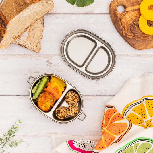 Ecococoon stainless steel Snack Pod Duo with two metal compartments and lid filled with food on a wooden surface with bread and a colorful towel.