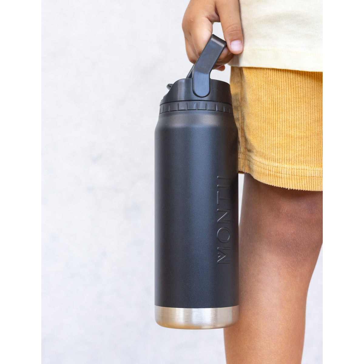 Person holding a MontiiCo black insulated water bottle with a silver base on a light gray background