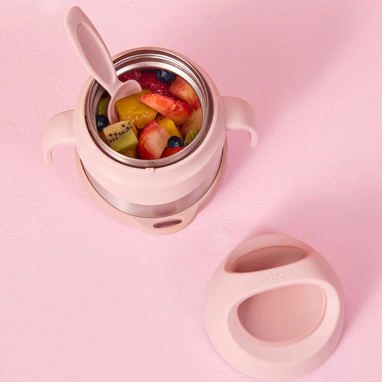 Pink children's lunchbox with fruit salad and a spoon on a pink background