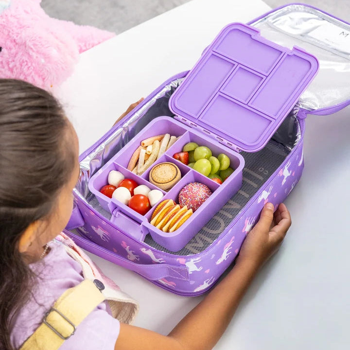 Child opening the packed purple MontiiCo Bento 5 Unicorn lunch box nested inside an insulated lunch bag on a table.