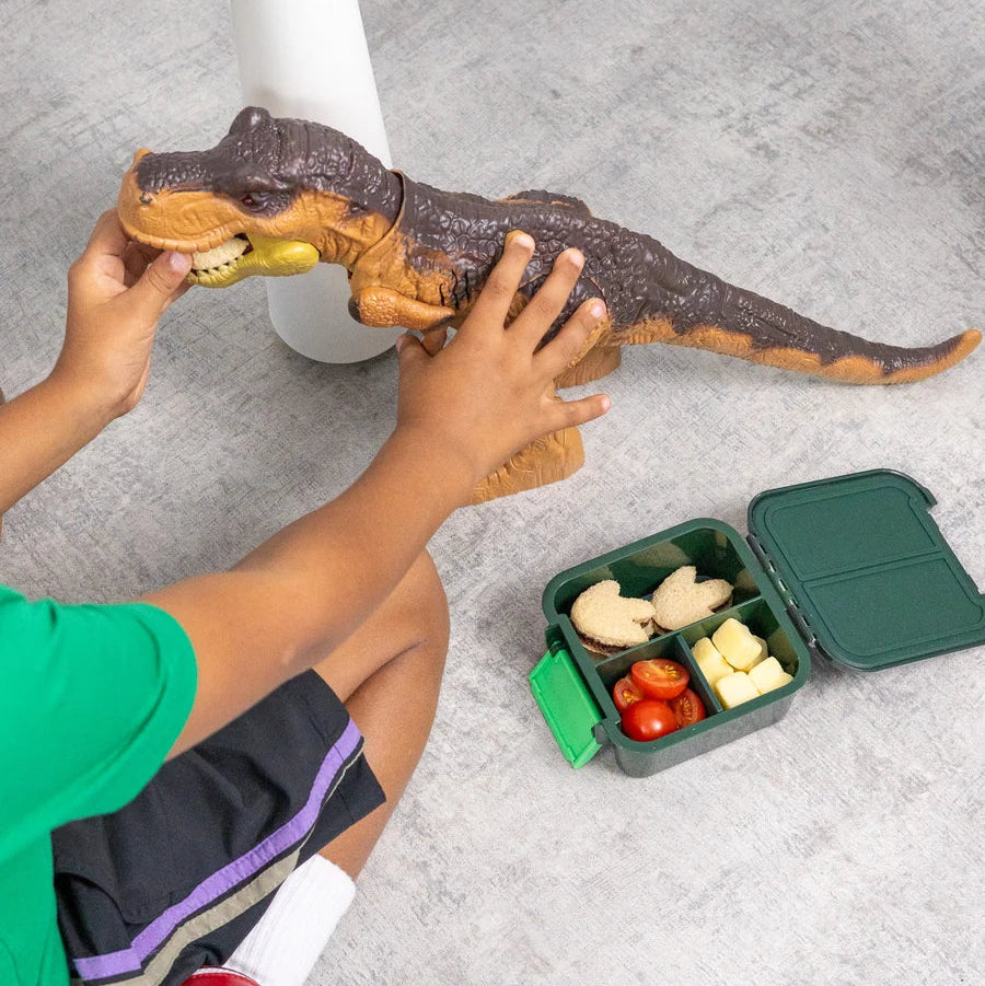 Child playing with a toy dinosaur on the floor next to an open MontiiCo Bento 2 packed snack box