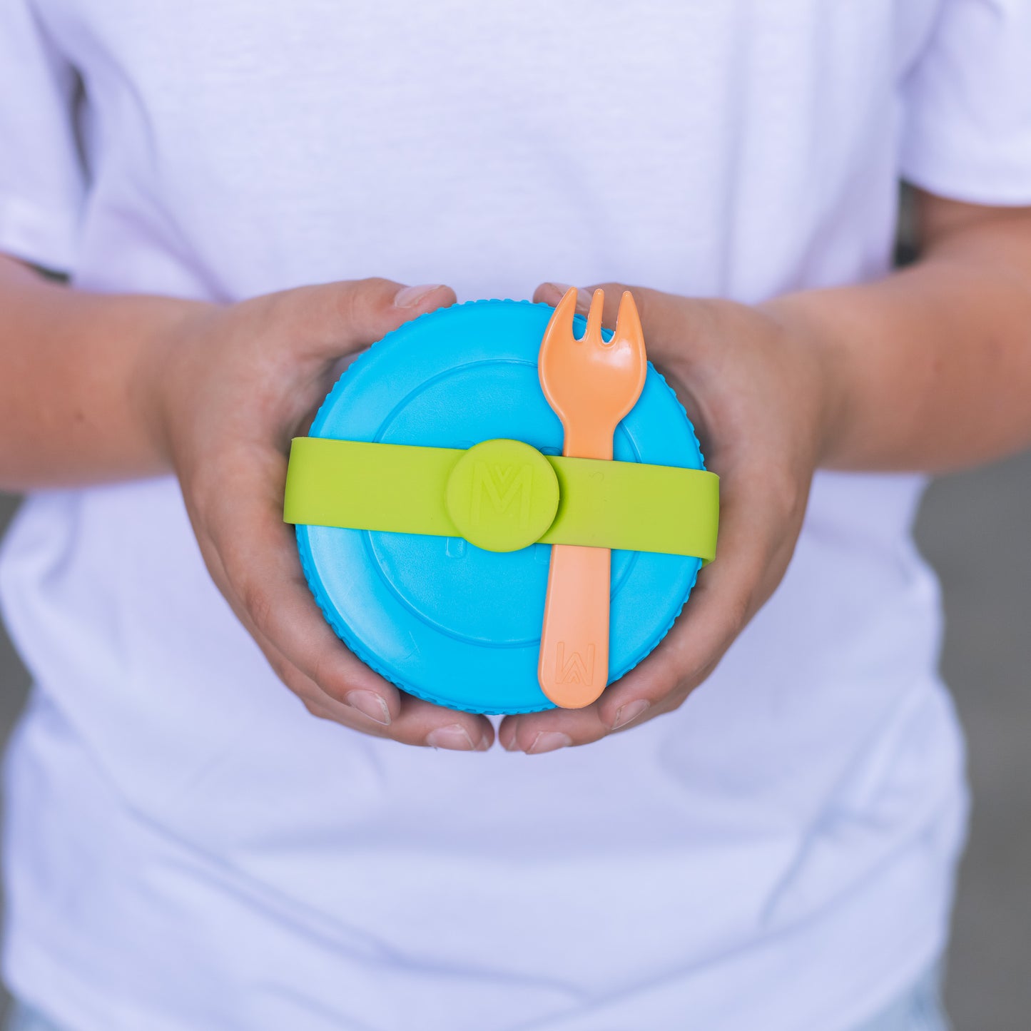 Child holding a blue lid with a green strap and orange fork against a white background