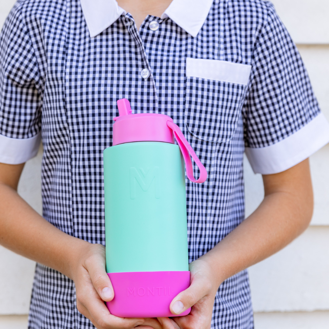 A child holding a Montii.Co Fusion Sipper Lid with a pink straw, checkered dress, and a white shirt.