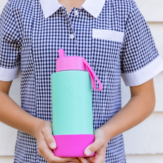 A child holding a Montii.Co Fusion Sipper Lid with a pink straw, checkered dress, and a white shirt.