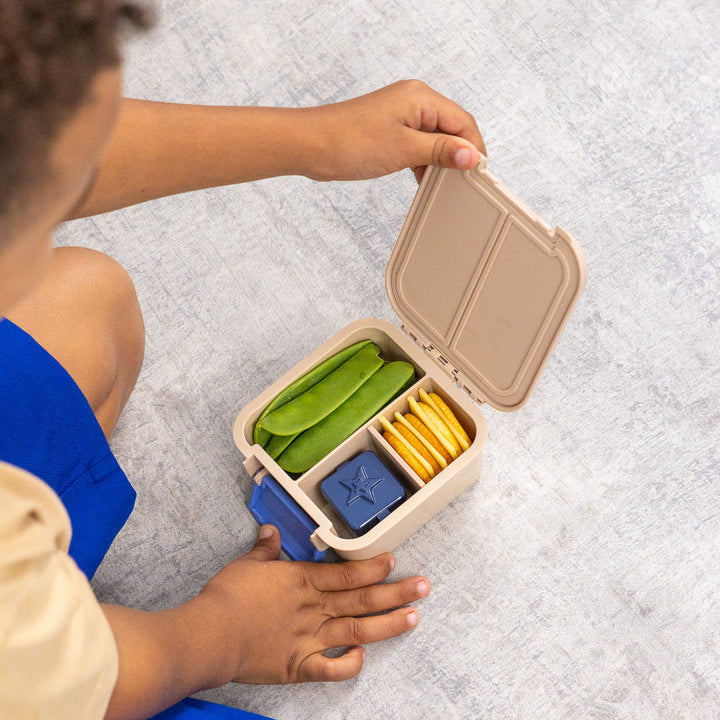 Child opening the packed beige MontiiCo Bento 2 Construction snack box on the floor