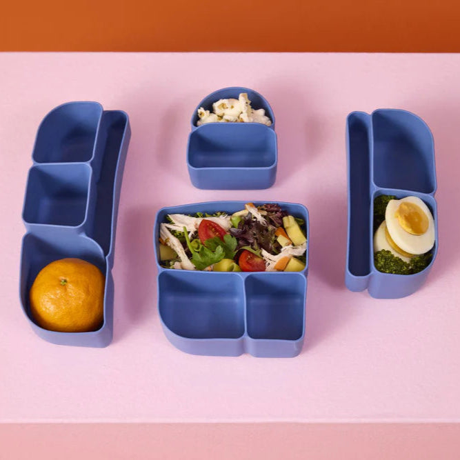 Blue b.box silicone insert bentocontainers with food items on a pink background