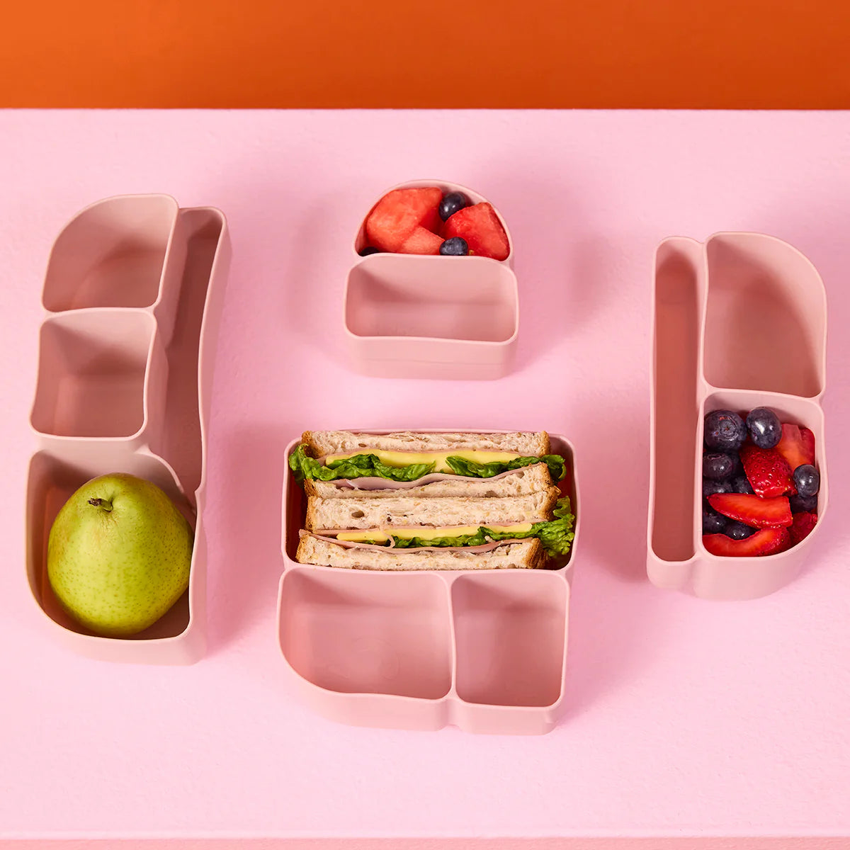 b.box Silicone Bento Tray : MINI -  Berry Pink divided lunch container with sandwich, apple, and fruit on a pink background