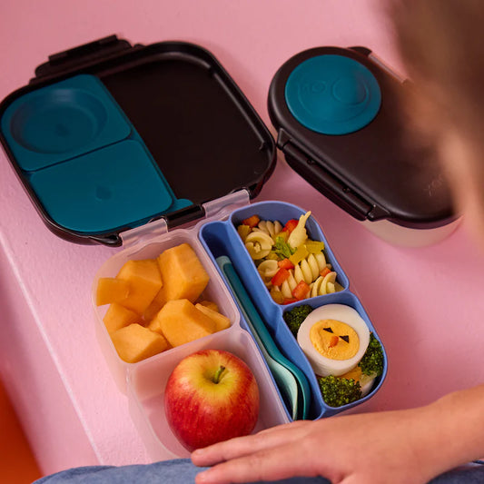 b.box Silicone Bento Tray : MINI - Ocean Bento box with compartments of fruits, vegetables, and a sandwich on a pink surface.