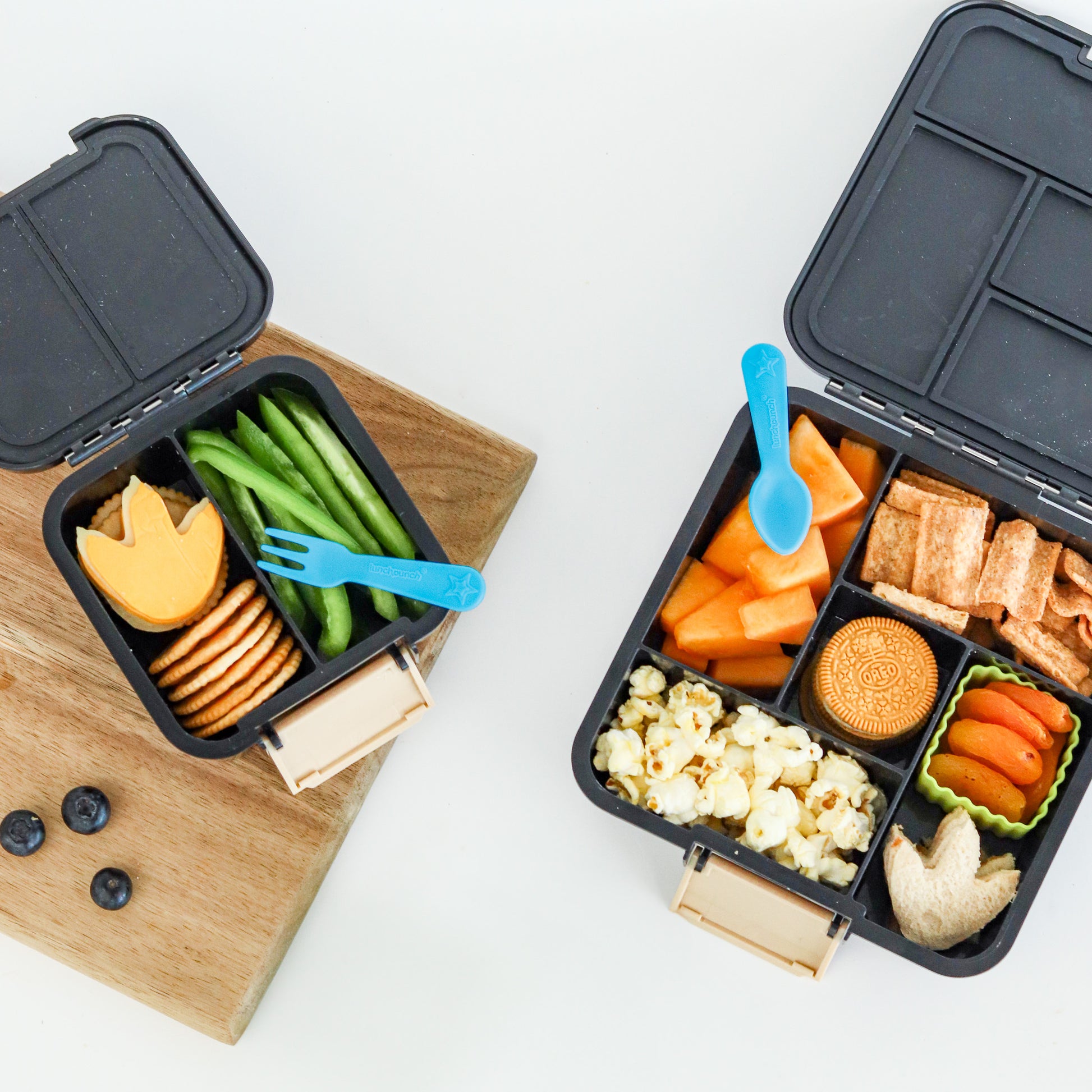 Two black bento boxes with compartments filled with snacks and vegetables on a white background.