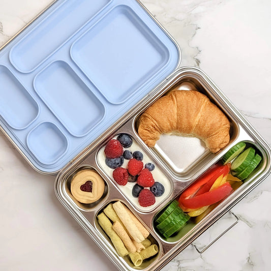 An open Ecococoon stainless steel leakproof bento box with five compartments, containing a variety of food items like fruits, vegetables, and a pastry. The box has a blue lid.