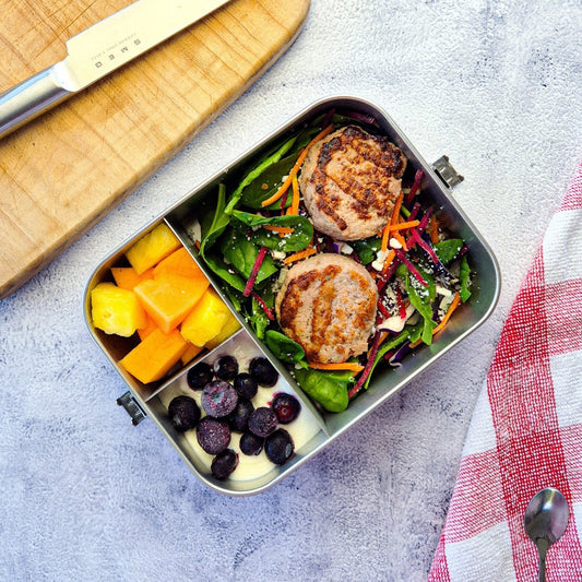 Ecococoon Bento 3 Metal lunch box with salad, fruit, and yogurt on a gray surface with a red checkered towel.