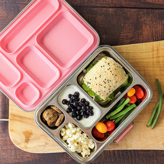 An open Ecococoon stainless steel leakproof bento box in pink rose color, displaying five compartments filled with various food items like a sandwich, fruits, and vegetables.