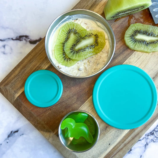 Ecococoon stainless steel snack pot with emerald green lid with kiwi slices on a wooden cutting board