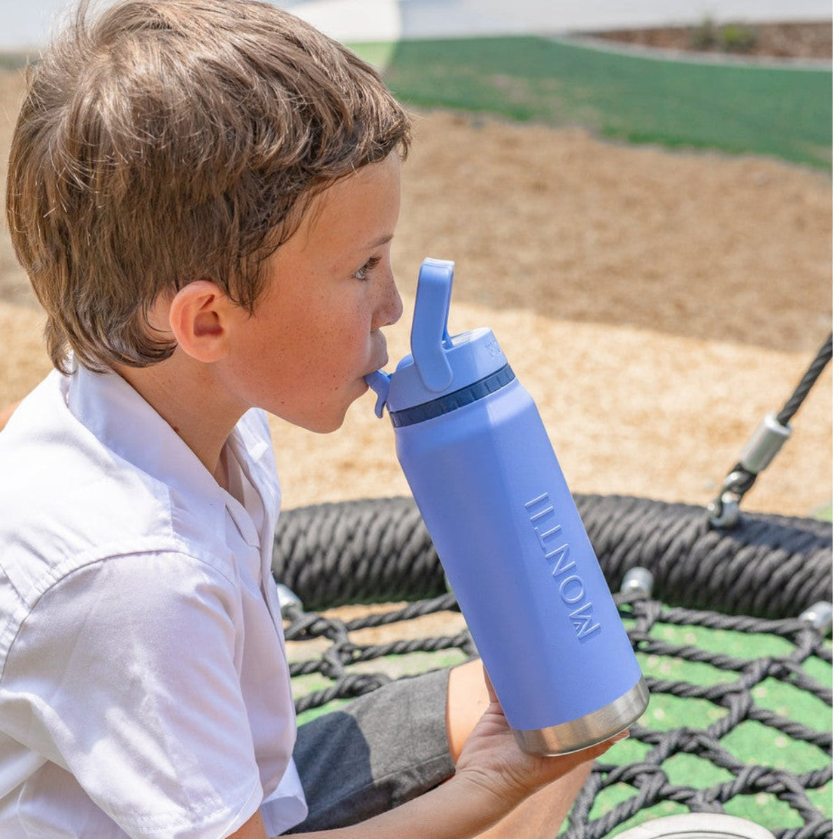 Child holding a blue Montii Co water bottle with a straw lid on a playground.
