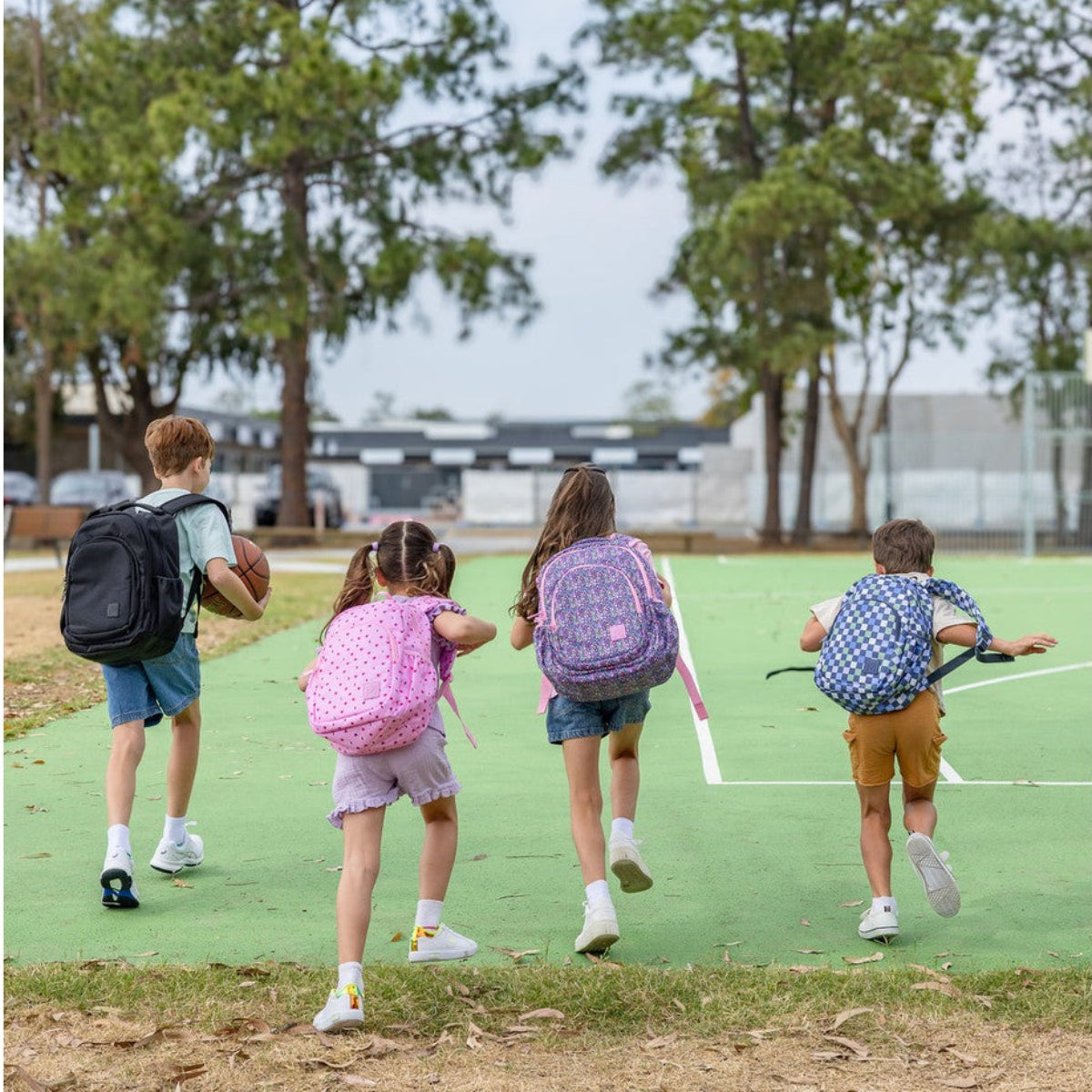 Four children running on a green field with trees in the background