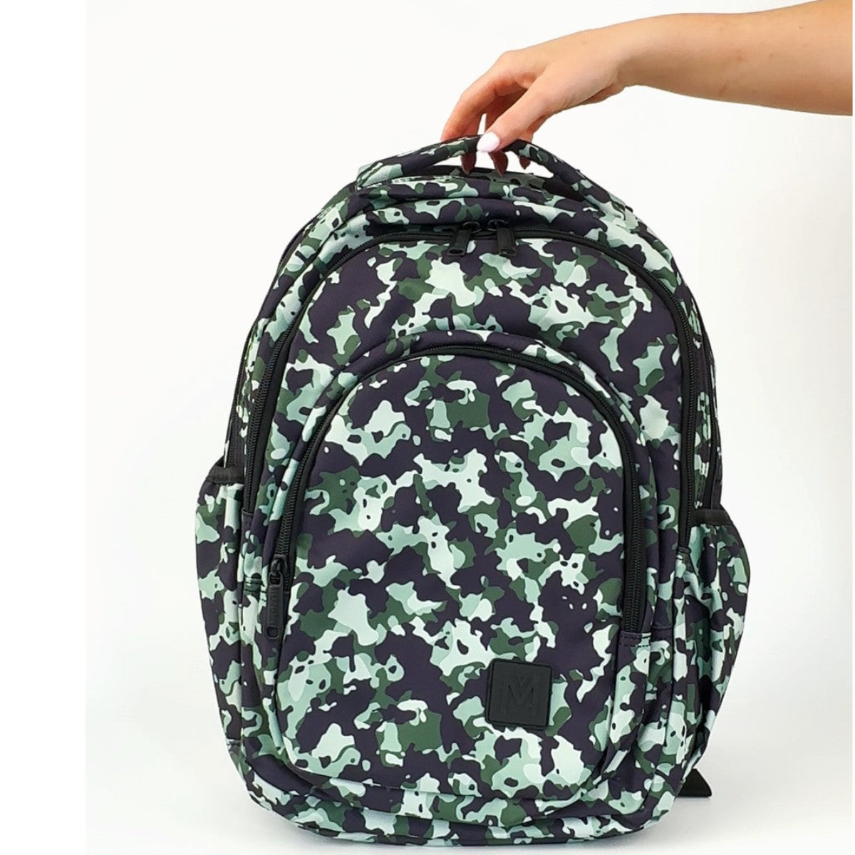 Camouflage MontiiCo Backpack - Stealth-patterned backpack held by a hand on a white background