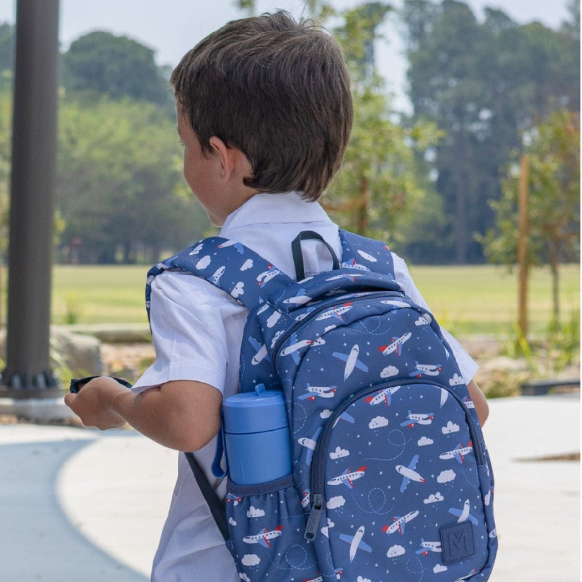 Child wearing a blue MontiiCo Mini Backpack with Jetset airplane pattern outdoors