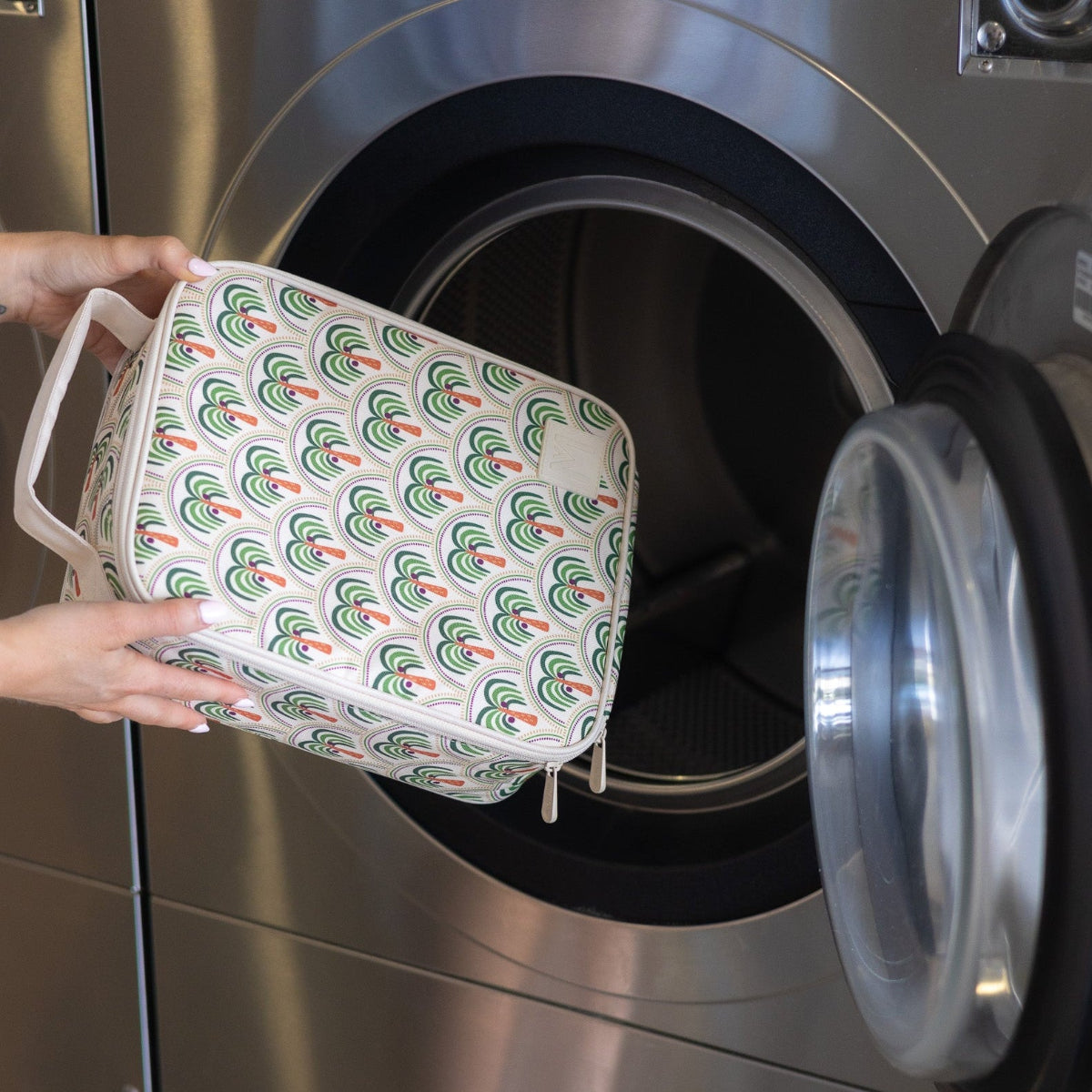 Person holding a Montii Co patterned fabric basket in front of an open washing machine.