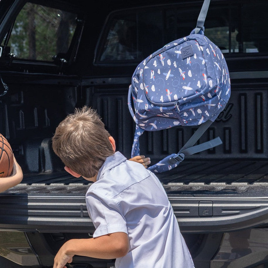 Child reaching into a car trunk with a blue backpack hanging from the rear of vehicle