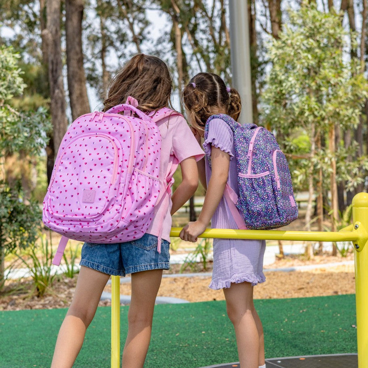Two children on a playground with pink and purple MontiiCo backpacks