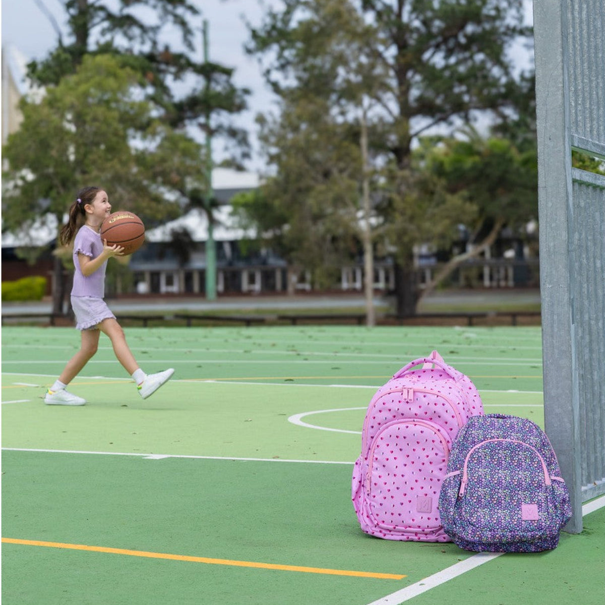 Girl holding a basketball on a court with two MontiiCo backpacks nearby