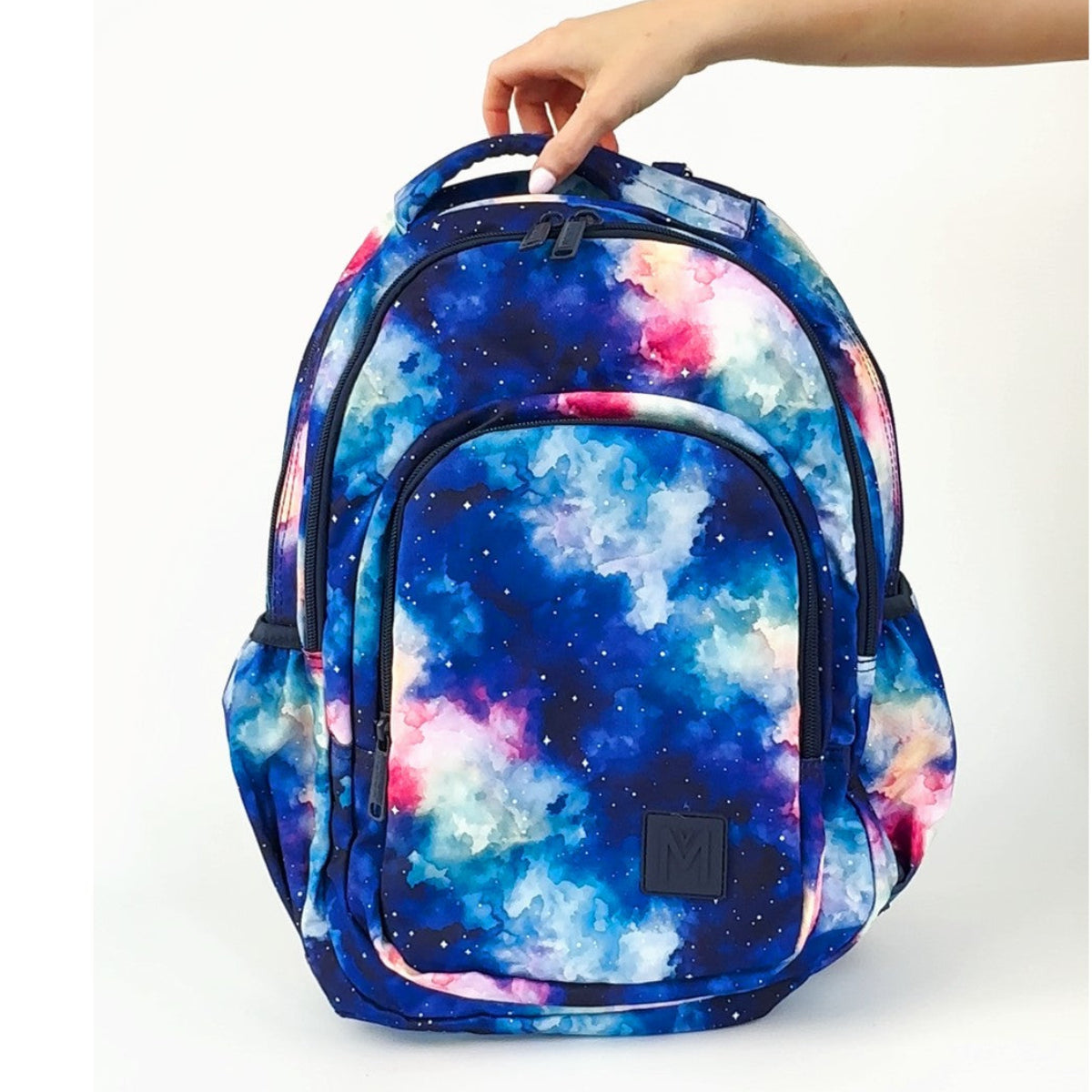 MontiiCo Starlight Backpack with a colorful galaxy design held by a hand on a white background