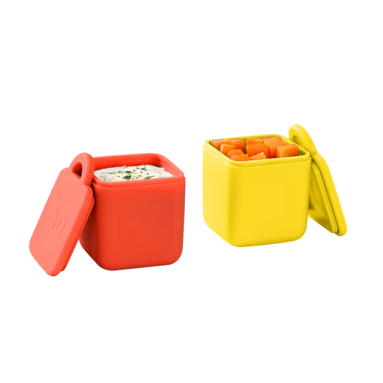 Two small square food containers, one red and one yellow, with lids, designed to be leakproof and used for packing dips or sauces.