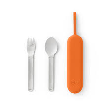 An orange flatware pod with a stainless steel fork on the left and a spoon on the right, designed to be attached to a bag or container.