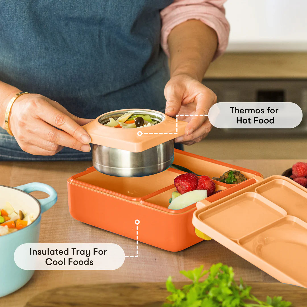 Preparing food in the Poppy Orange OmieBox V2 leakproof bento lunch box with divided compartments.