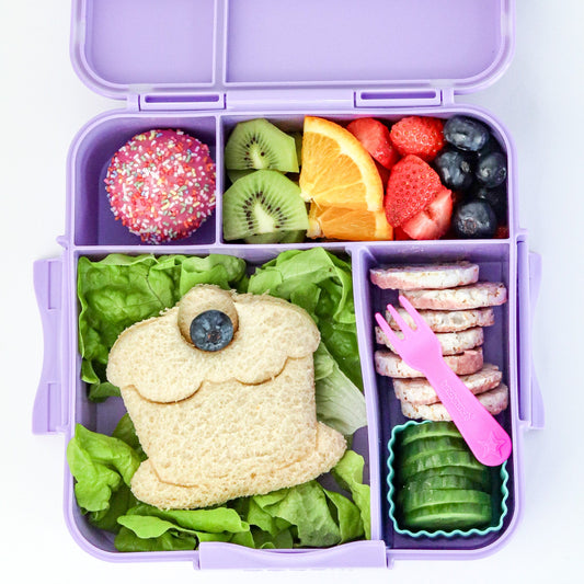 Purple bento box with a variety of food including a sandwich shaped like a frog, fruits, and vegetables.