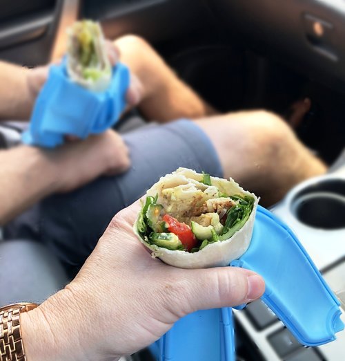 Two people eating wraps in a car using blue Wrap’d silicone wrap holders, showing reusable wrap holders that keep wraps, sandwiches and tortilla wraps secure and mess‑free while eating on the go.