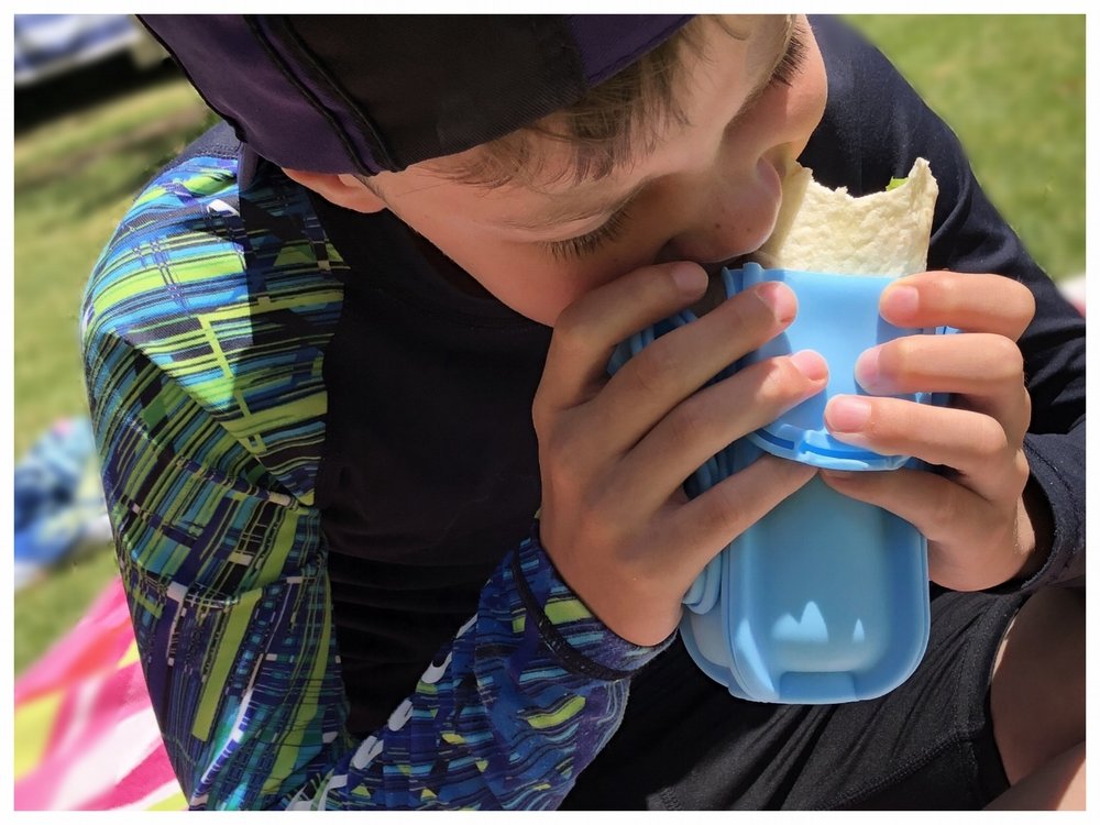 Child eating a burrito held in a blue Wrap’d silicone wrap holder, showing a reusable wrap holder that keeps wraps and tortilla wraps secure and easy for kids to eat.